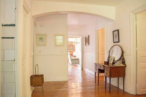 A hallway with a wooden floor, white walls, a wooden dresser with a mirror, and framed pictures.