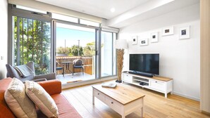Ein modernes Wohnzimmer mit Sofa, Fernseher, Couchtisch und einer Schiebeglastür, die zu einem Außenbereich führt.