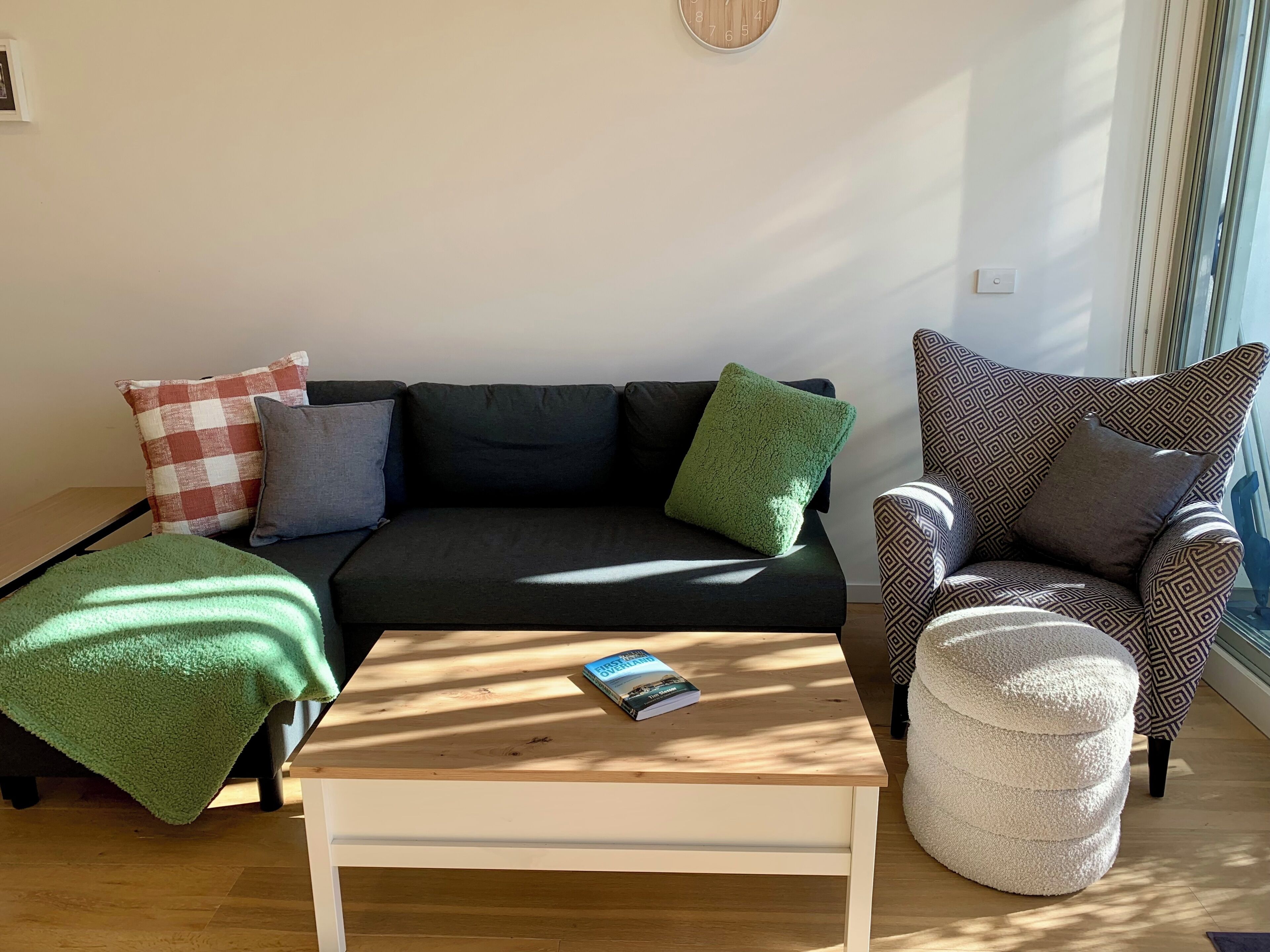 Una sala de estar con sofá, sillón, reposapiés y una mesita de centro con un libro.