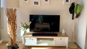 Ein Wohnzimmer mit Fernseher, gerahmten Bildern, einer Lampe, einer Pflanze und einem Schuhregal.