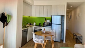 Eine kompakte Küche mit weißen Schränken, einer grünen Spritzschutzwand, einem Edelstahlkühlschrank und einem Essbereich mit weißen Stühlen.