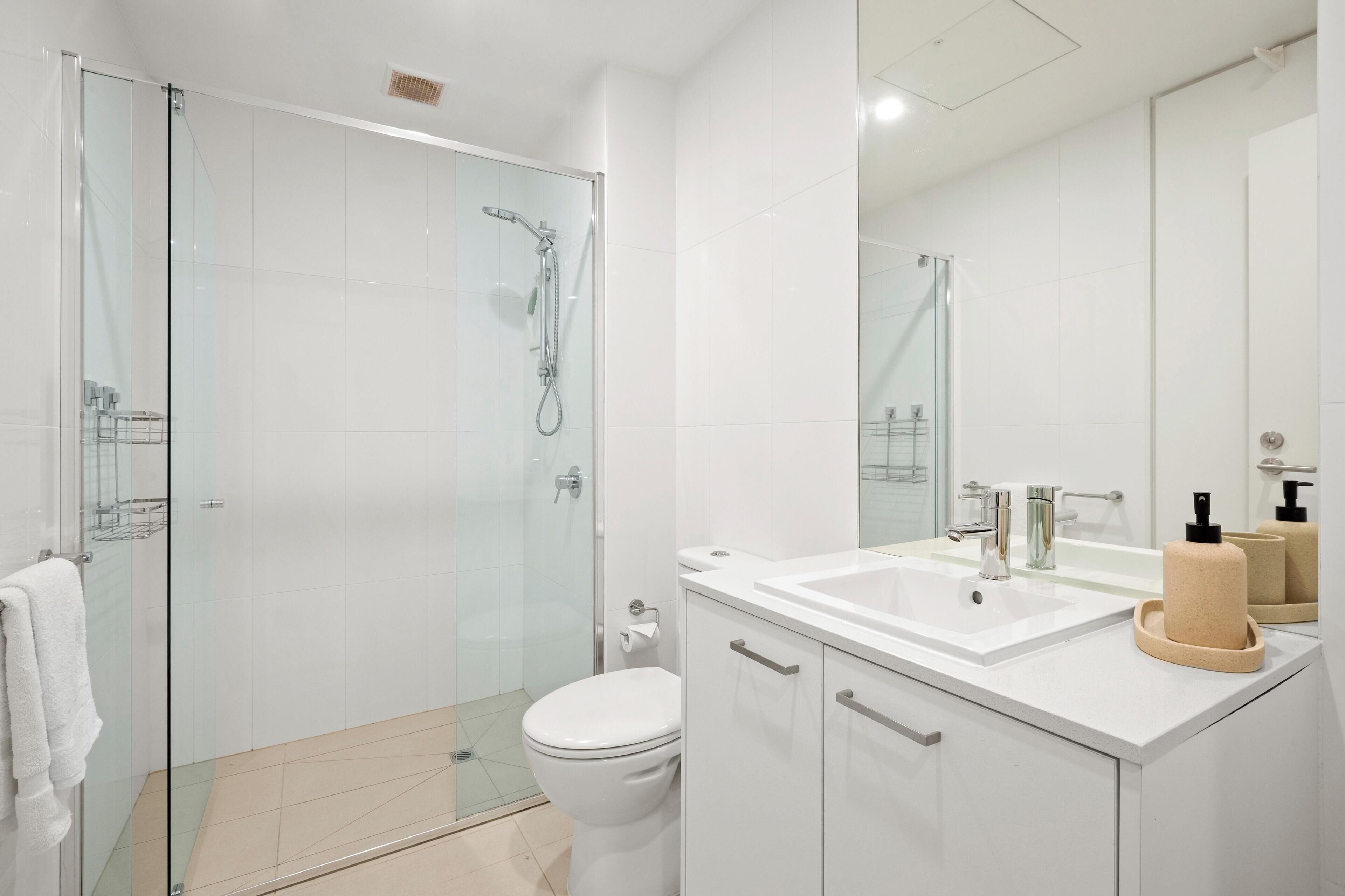 A modern bathroom with a glass-enclosed shower, a white toilet, a sink with a mirror, and a towel rack.