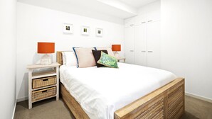 Ein Schlafzimmer mit Bett, Nachttischen, Korbwäsche, einem Kleiderschrank und gerahmten Bildern an der Wand.