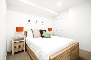 Ein Schlafzimmer mit Bett, Nachttischen, Korbwäsche, einem Kleiderschrank und gerahmten Bildern an der Wand.