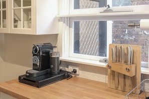 Une cuisine équipée d’une machine à café, d’un bloc à couteaux et d’une fenêtre donnant sur un mur de briques.