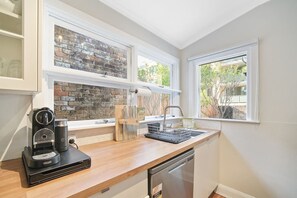 A kitchen with a brick backsplash, a coffee maker, a dishwasher, and a window with a view of greenery.