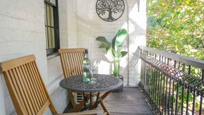 Een balkon met een ronde tafel, twee houten stoelen, een bloempot en een muurschildering van een boom.
