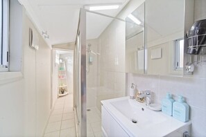 A modern bathroom with a glass shower enclosure, a white sink with toiletries, and a mirror.
