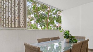 A dining area with a glass-top table, wicker chairs, a potted plant, and a view of trees and buildings through a window. - Spacious Mascot 2BR Near Airport + Parking/Pets (Mascot)