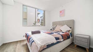 A modern bedroom with a large bed, a nightstand, and a window with a city view. - Spacious Mascot 2BR Near Airport + Parking/Pets (Mascot)