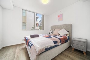 Ein modernes Schlafzimmer mit einem großen Bett, einem Nachttisch und einem Fenster mit Blick auf die Stadt.