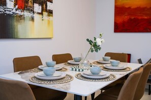 Ein Esstisch ist gedeckt mit blauen Schüsseln und Tellern, umgeben von Stühlen, mit einer Blumenvase und einem Gemälde an der Wand.