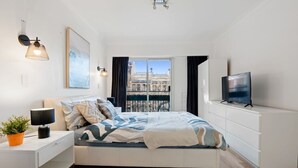Et moderne soveværelse med seng, sengebord, lampe, fjernsyn og et vindue med udsigt over byen.