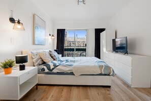 A modern bedroom with a bed, bedside table, lamp, TV, and a window with a city view. - Apartment in Potts Point+Parking (Potts Point)
