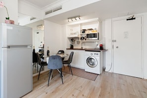 A compact kitchen with a refrigerator, microwave, and washing machine, a dining area with chairs, and a door with a lock. - Apartment in Potts Point+Parking (Potts Point)