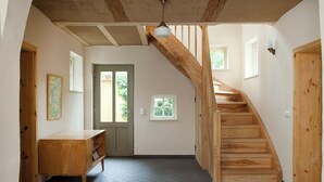 A spacious room with a herringbone floor, a wooden staircase, and a door leading to another area.