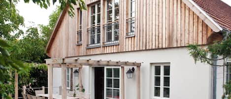 A two-story wooden house with a covered patio, outdoor seating, and a garden.
