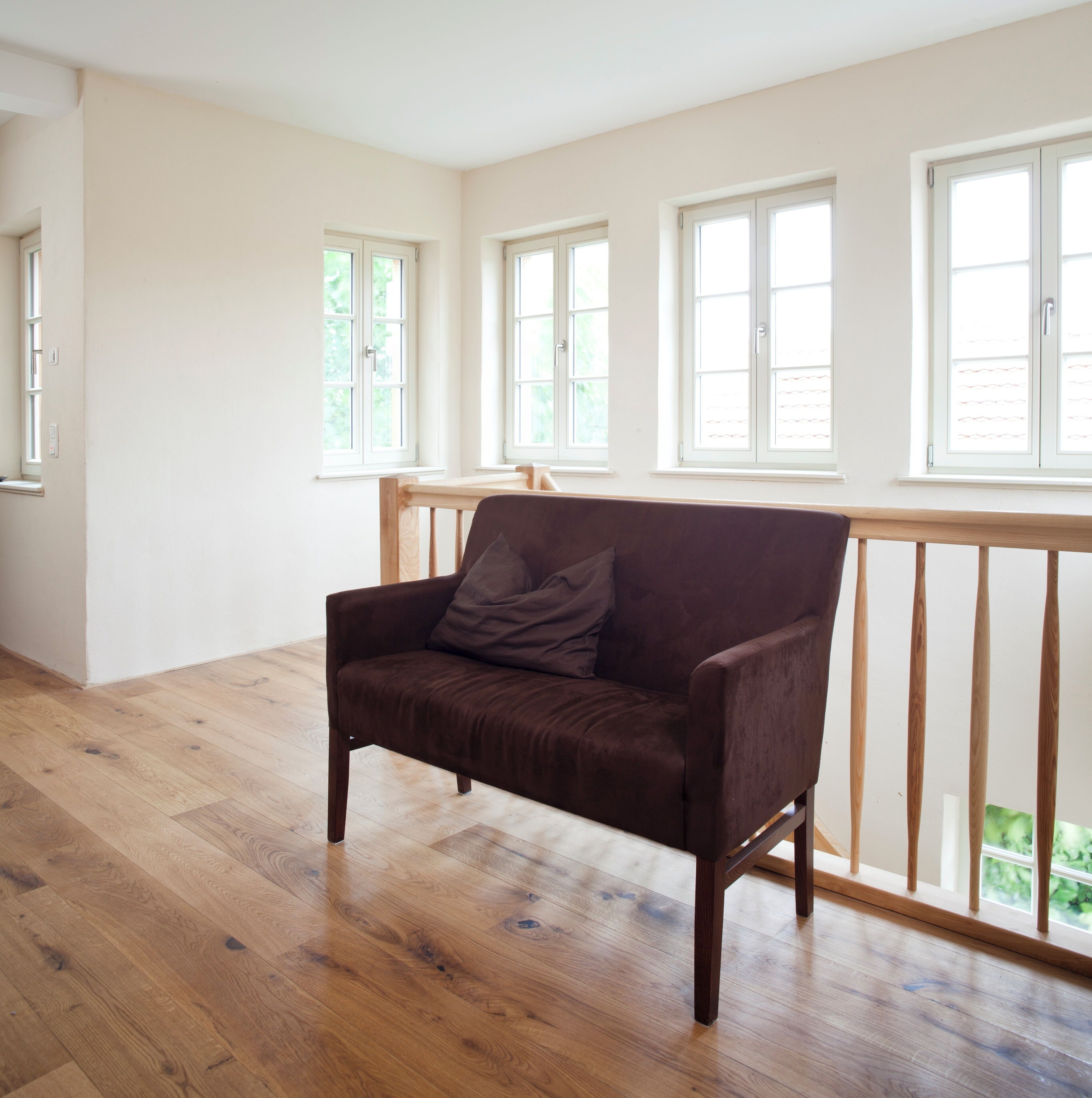 Een kamer met een houten vloer, een bruine bank en een raam met een witte omlijsting.