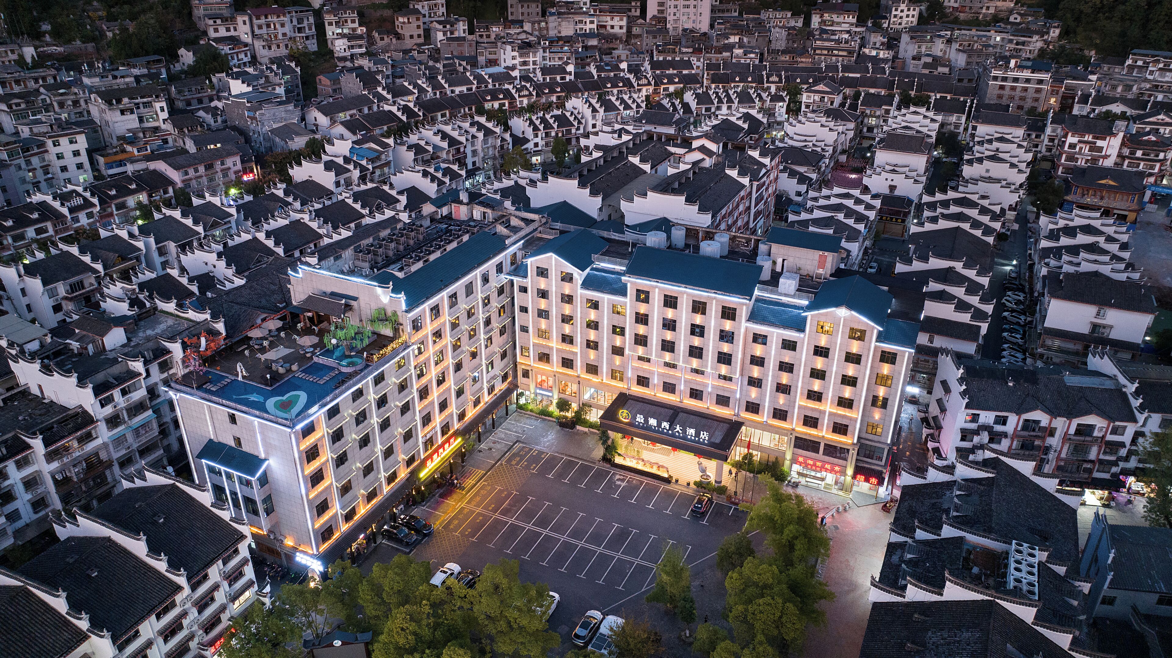 An aerial view of a hotel with a parking lot, surrounded by traditional-style buildings.