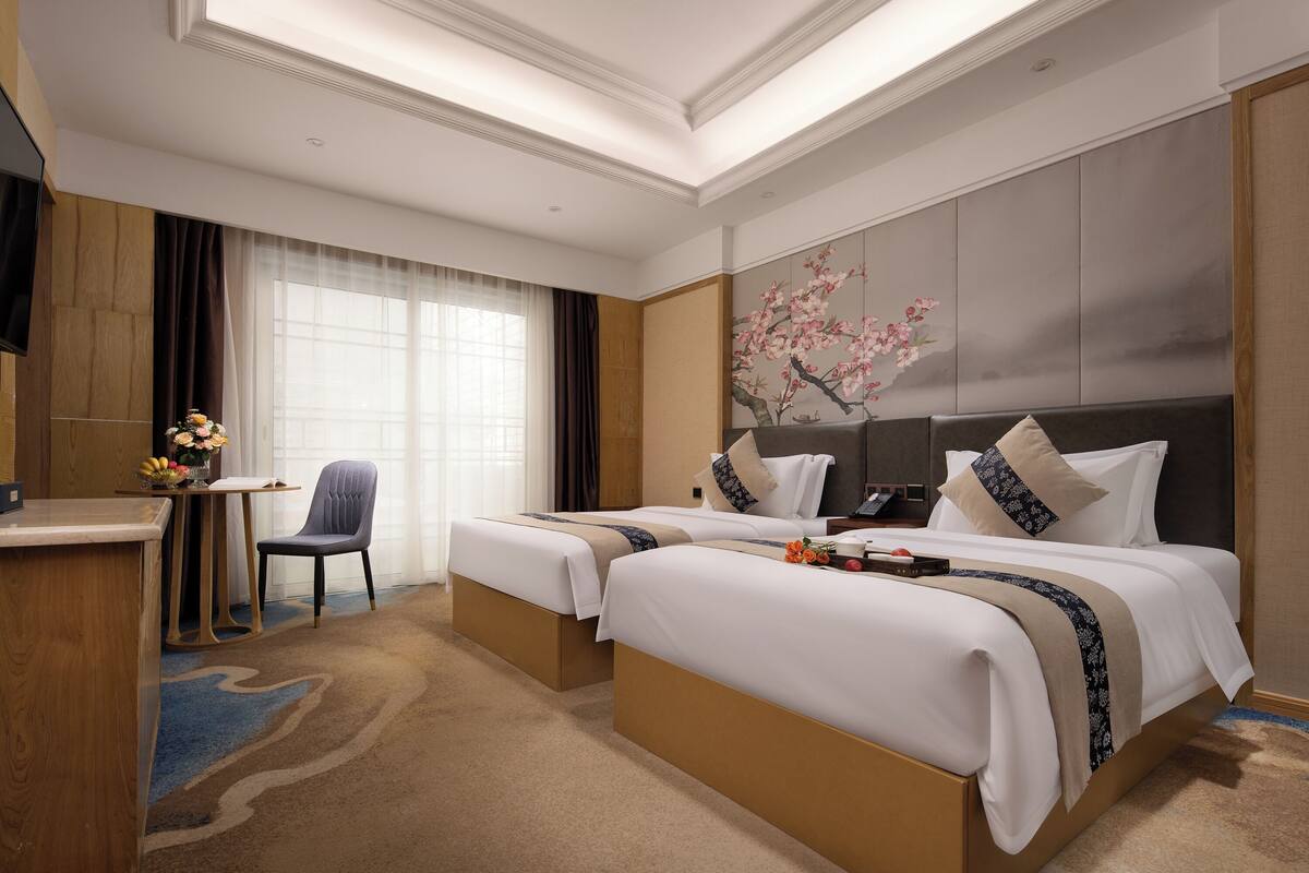 A hotel room with two beds, a desk, a chair, and a large window with curtains.