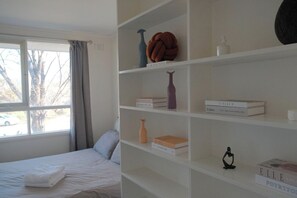 Ein Schlafzimmer mit einem Bett, einem Fenster mit Vorhängen, einem Bücherregal mit Büchern und Dekoration.