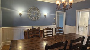 Ein Esszimmer mit Holztisch und -stühlen, einer Wanduhr und einem Kronleuchter.