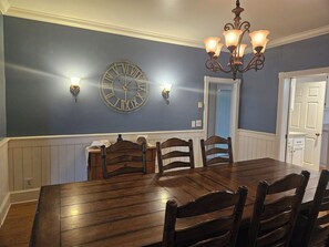 A dining room with a wooden table and chairs, a wall-mounted clock, and a chandelier. - Farmhouse Retreat Near Yellowstone National Park Perfect for Groups (Gardiner)