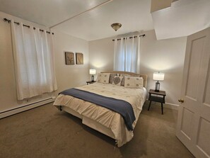A bedroom with a bed, two bedside tables, a heater, and a door. - Farmhouse Retreat Near Yellowstone National Park Perfect for Groups (Gardiner)