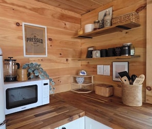 A compact kitchen with wooden walls, a coffee press, a microwave, and various kitchen utensils on shelves. - Lakeview Property on Indian Lake NB Canada (Sheffield)