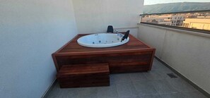 Ein Whirlpool auf einem Balkon mit Blick auf Gebäude und Hügel.