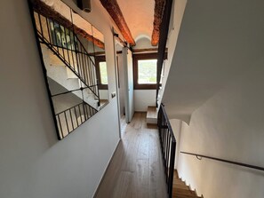 Un couloir étroit avec un escalier en bois, une rampe en métal et une fenêtre laissant entrer la lumière naturelle.
