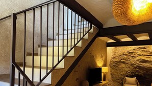 A staircase with a metal railing leading to a room with a stone wall, a television, a lamp, and a chair. - Lo Mirador de les Roques, a rural house with spectacular views (Benifallet)