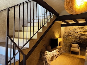 A staircase with a metal railing leading to a room with a stone wall, a television, a lamp, and a chair.