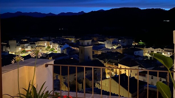 A balcony with a view of a cityscape at dusk, potted plants, and a bamboo ceiling. - Lo Mirador de les Roques, a rural house with spectacular views (Benifallet)
