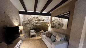 A modern living room with a stone wall, a sofa, a chair, and a TV. - Lo Mirador de les Roques, a rural house with spectacular views (Benifallet)