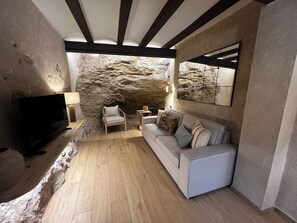 Un salon moderne avec un mur en pierre, un canapé, un fauteuil et un téléviseur.
