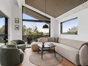 Ein modernes Wohnzimmer mit einem großen Fenster, einem Sofa, einem Couchtisch und zwei Sesseln.