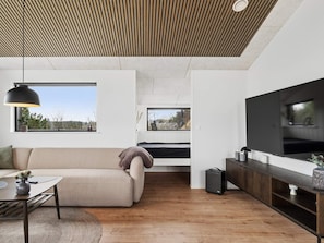 Uma sala de estar moderna com sofá, mesa de jantar, televisão e teto de madeira.