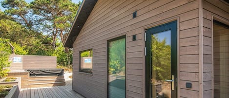 A modern wooden cabin with a deck, large sliding glass doors, and a small window.