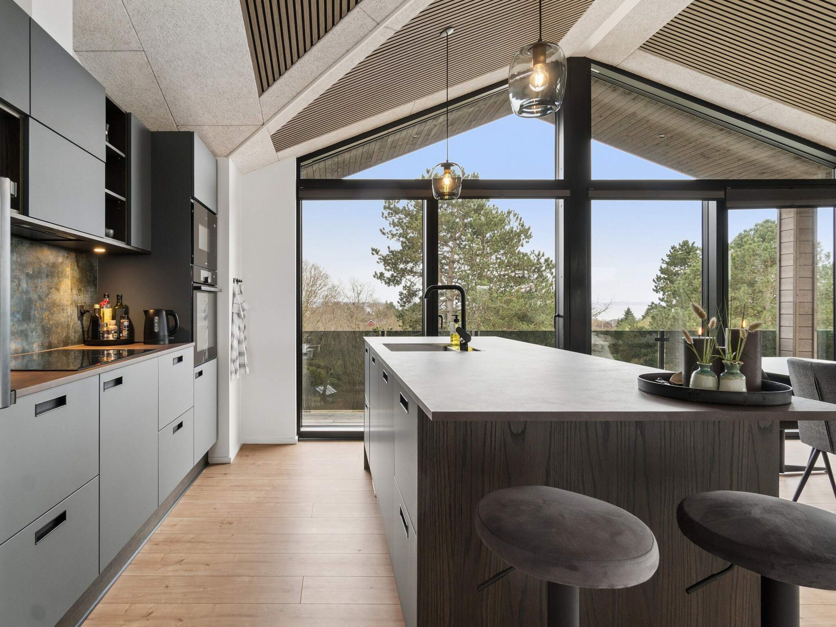 A modern kitchen with a large island, bar stools, and a view through large windows.