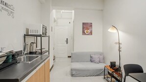 Un espacio habitable pequeño con kitchenette, un sofá, una mesa de centro y una lámpara de pie.