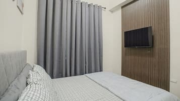 A bedroom with a bed, grey curtains, a mounted TV, and a wooden wardrobe.