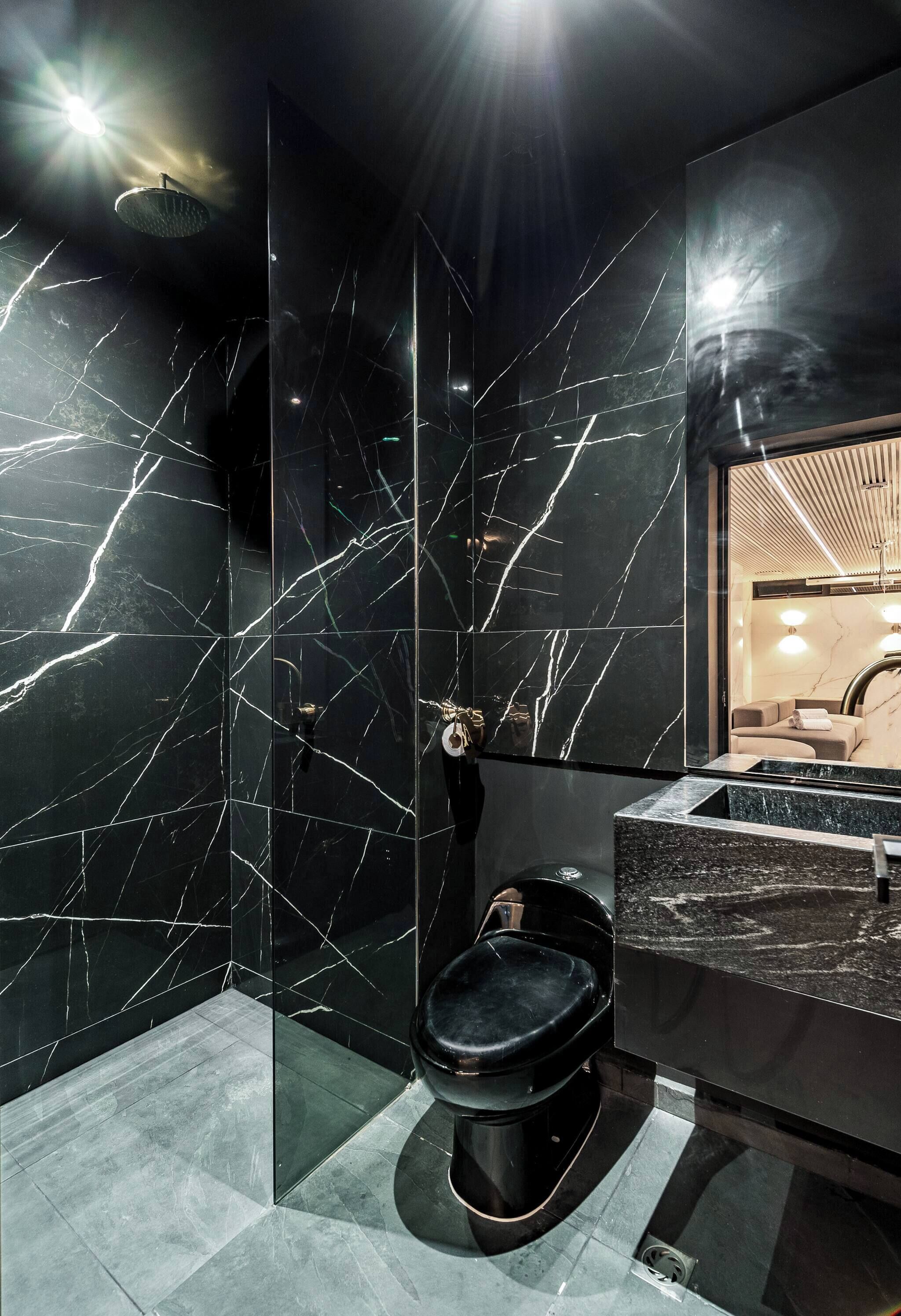 A modern bathroom with a black marble wall, a glass shower enclosure, and a black toilet.
