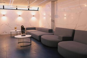 Eine moderne Lounge mit Ecksofa, runden Tischen und Marmorwänden.