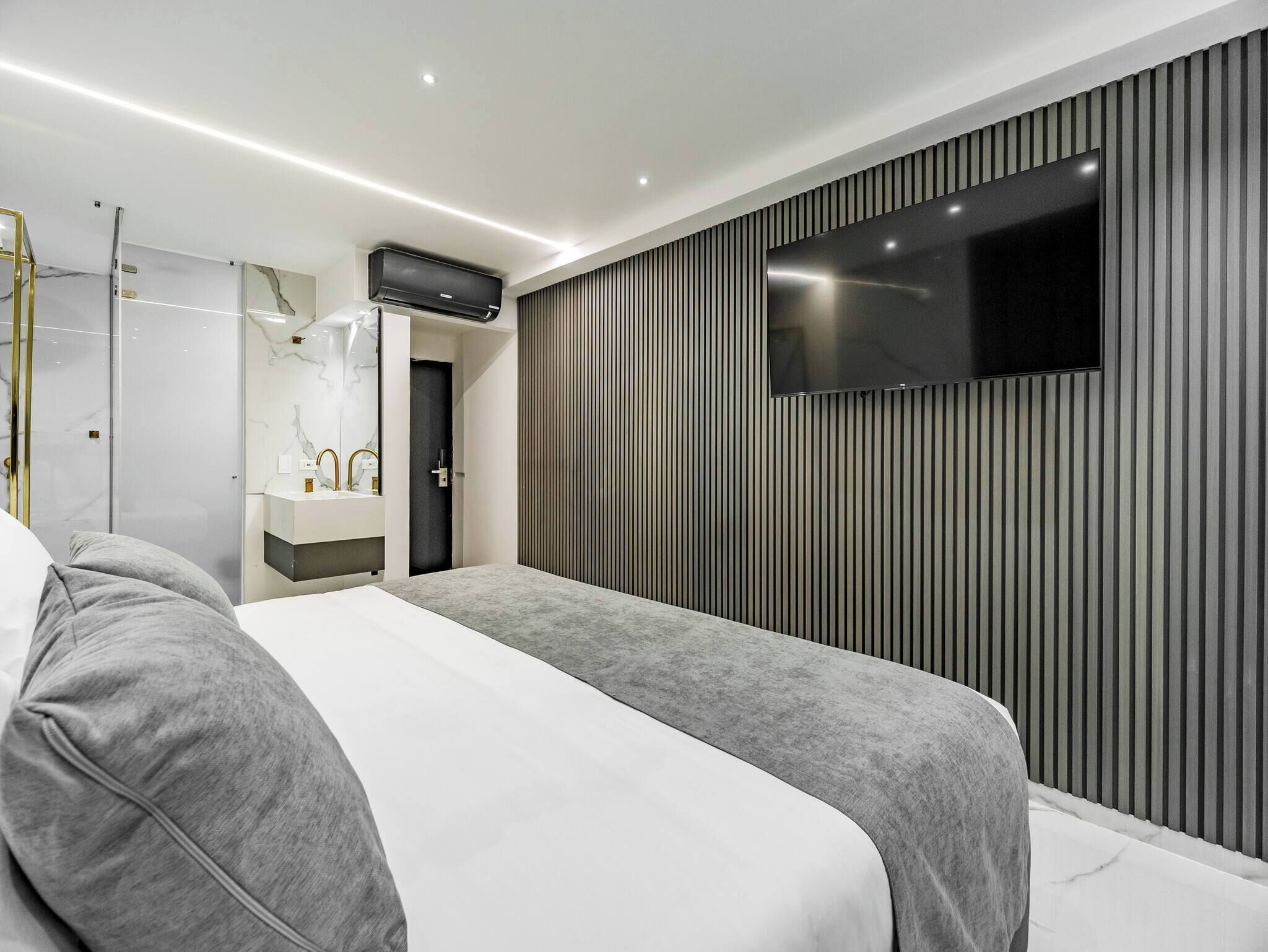 A modern hotel room with a large bed, a TV mounted on the wall, and a bathroom with a mirror and sink.