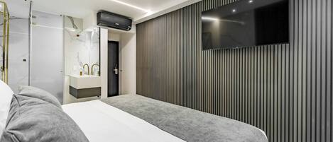 A modern hotel room with a large bed, a TV mounted on the wall, and a bathroom with a mirror and sink.
