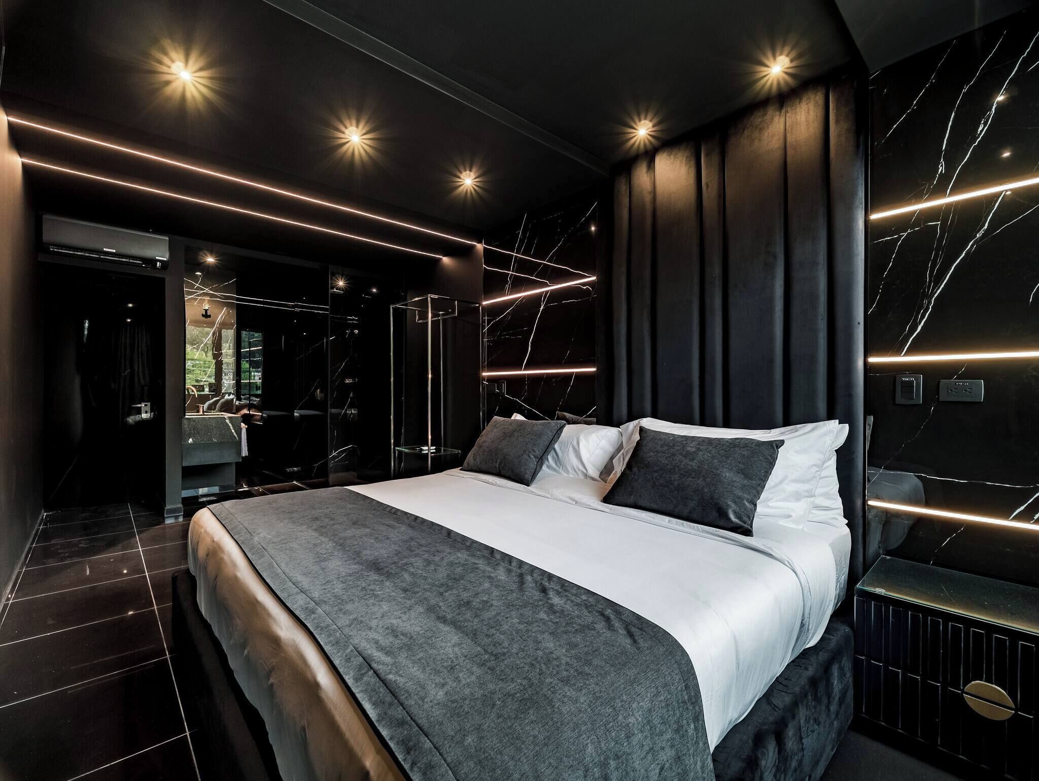 A modern bedroom with a large bed, dark walls, and a mirror.