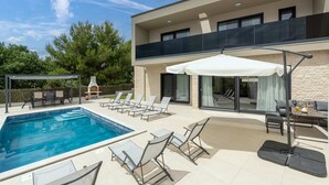 Ett modernt hus med en swimmingpool, utomhusmöbler och en täckt uteplats.