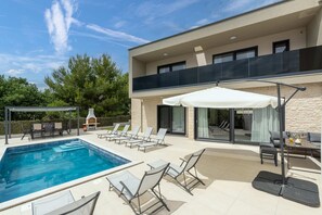 Ein modernes Haus mit Schwimmbad, Sitzgelegenheiten im Freien und einer überdachten Terrasse.