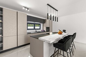 Eine moderne Küche mit Marmorarbeitsplatte, schwarzen Stühlen und einer Obstschale.